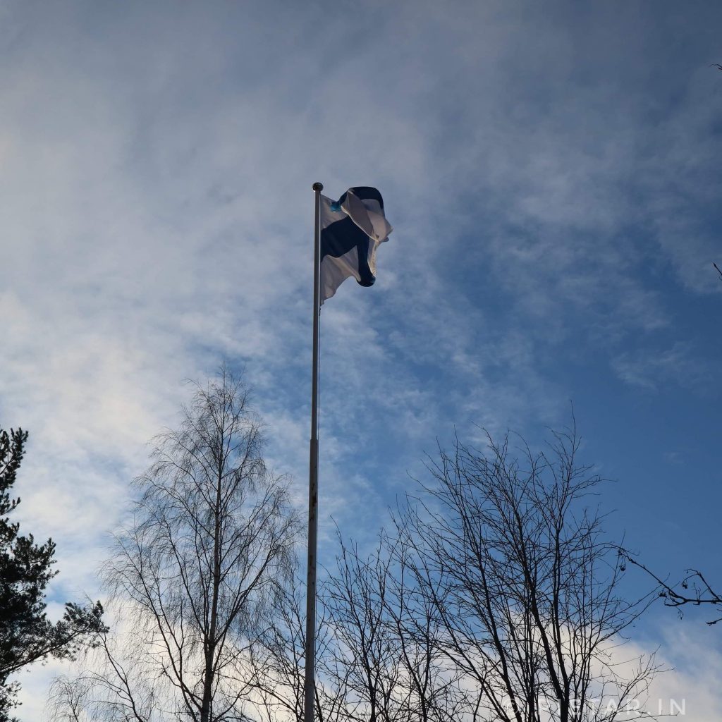 Suomen lippu sini-valkoista taivasta vasten.