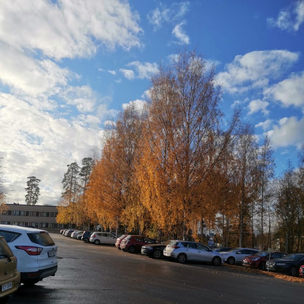 Aurinkoa, pilviä ja ruskaa terveyskeskuksen parkkipaikalla.