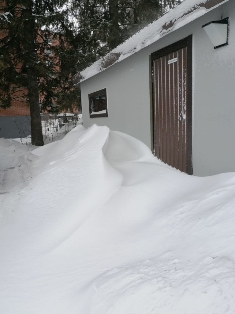 Pyörävaraston oven edessä on paljon lunta.