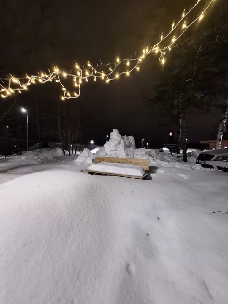 Muumipeikon näköinen lumikasa on penkin takana.